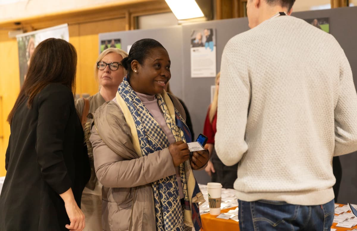 People chatting at an event stand, one smiling and holding a small card.