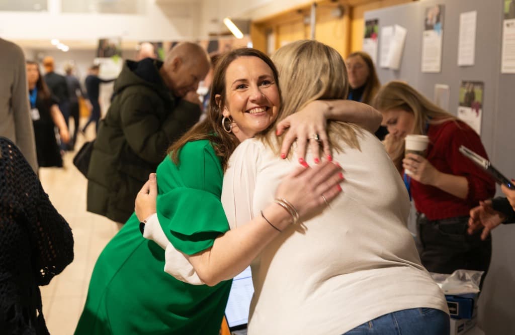 Two people share a warm hug at a busy event.